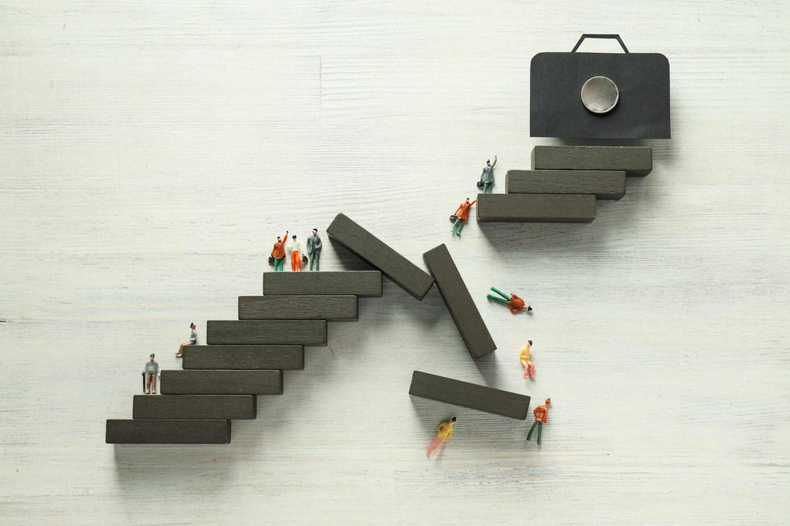 Small figures climbing concrete steps towards a briefcase