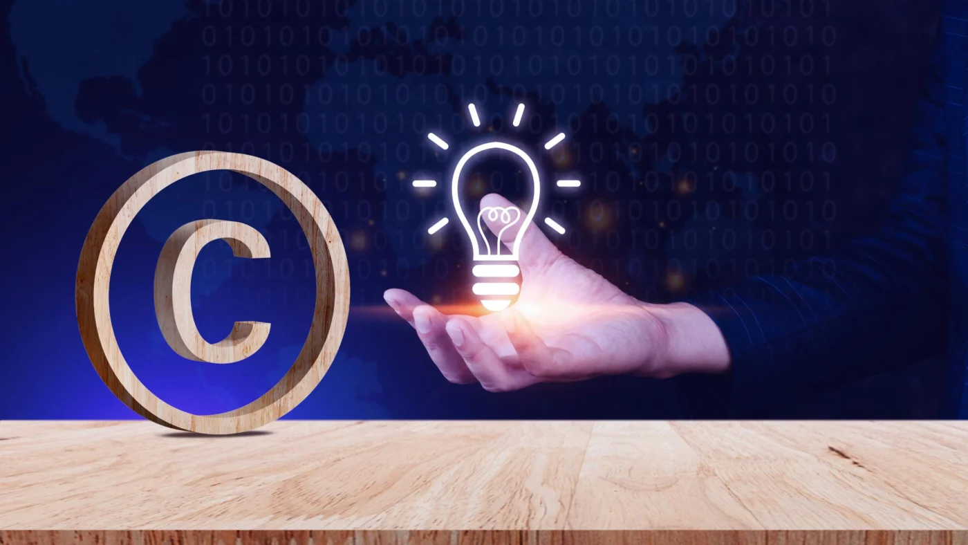 A copyright symbol and an illuminated lightbulb icon on a wooden desk, representing intellectual property rights
